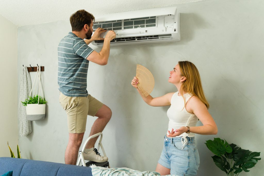 Young couple inspecting failing home air conditioning unit while cooling off indoors in Orlando Florida by English Air.
